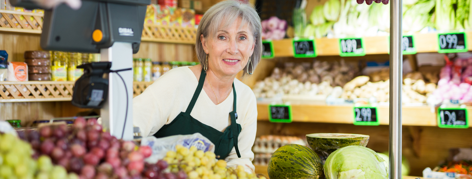 older woman standing behind grocery checkout counter with produce in front of her
